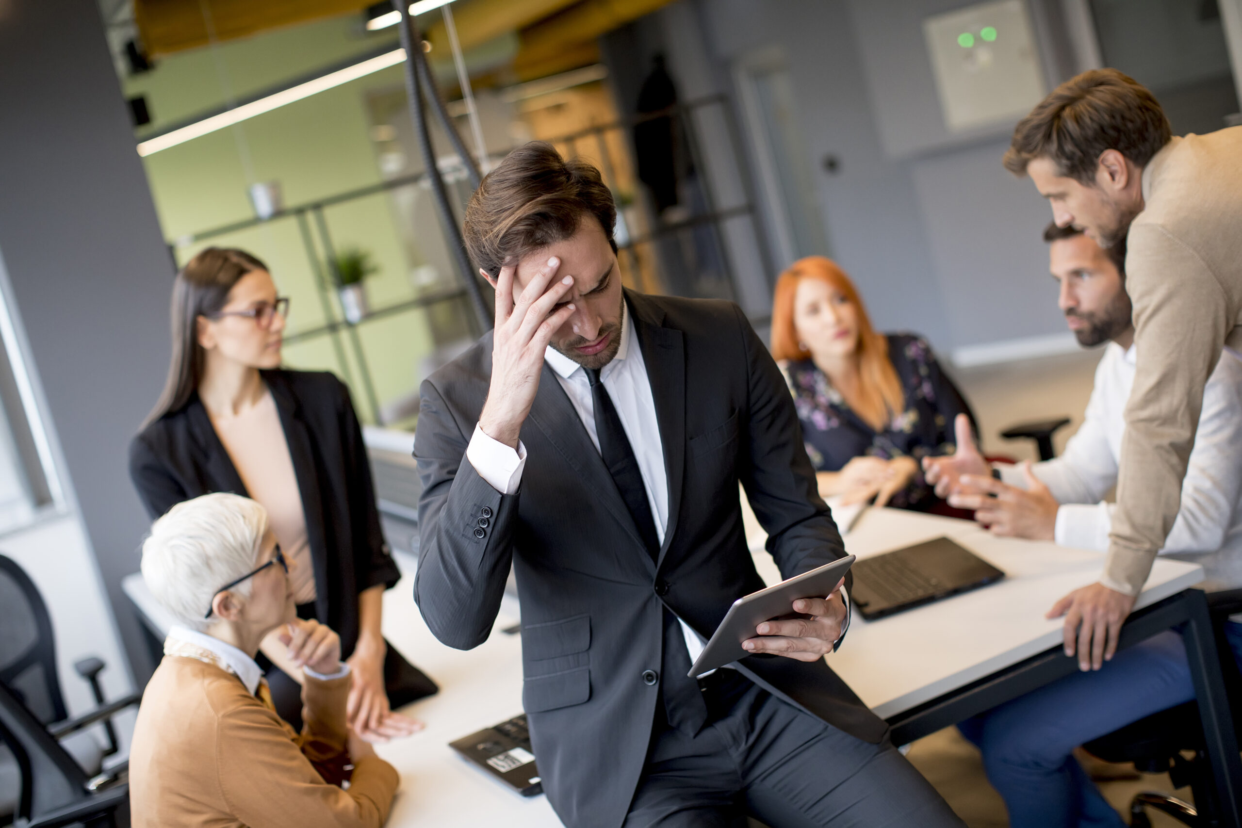 A young business professional stressed out with his team brainstorming in the background.