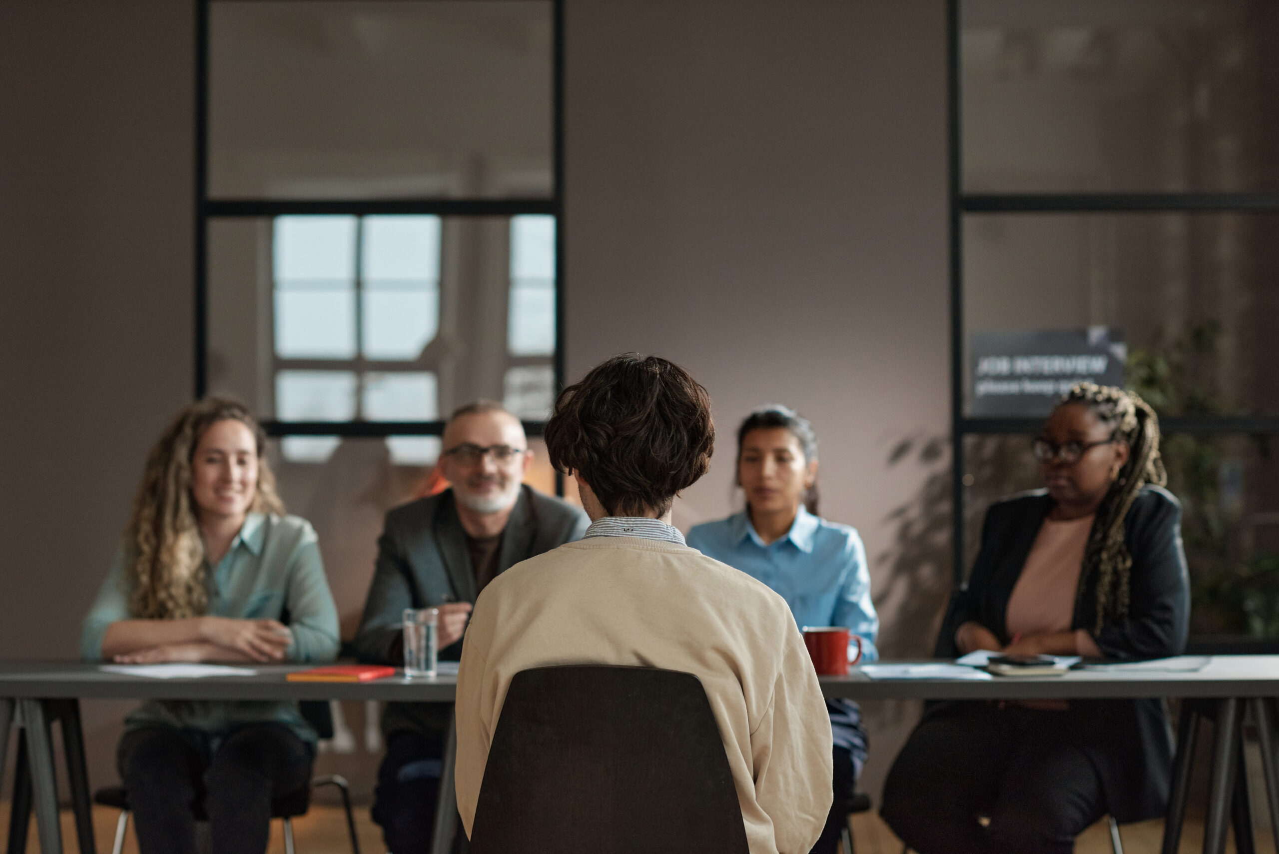 A job applicant sitting in front of a panel of interviewers in a modern office setting.